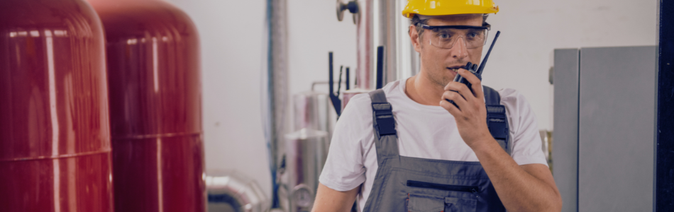 Worker wearing safety goggles talking on a walkie talkie with a boiler pressure in the background 