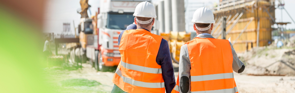 two workers on a construction site with a truck in the background.