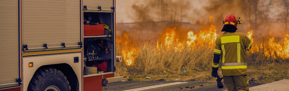firefighter walking towards a bushfire with a fire truck to his left.