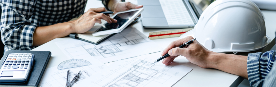 engineers working at a desk with a blueprint documents and a calculator scattered across