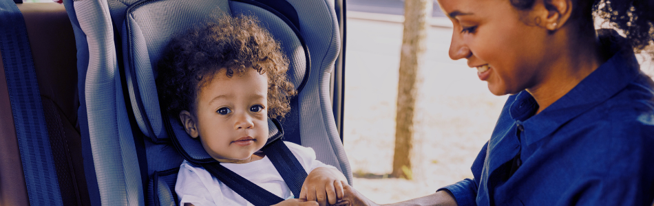 smiling adult putting child in childseat in a car